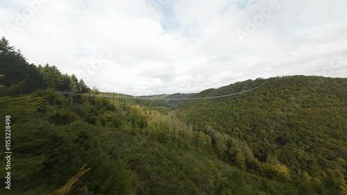 POV drone over forest trees at the Geierlay suspension bridge in Morsdorf, Germany under cloudy sky photo