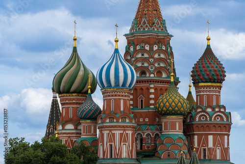St. Basil's Cathedral rises above Red Square against backdrop of blue sky. Cathedral towers are topped with multi-colored domes with Orthodox crosses. Walls of cathedral are made of red brick.