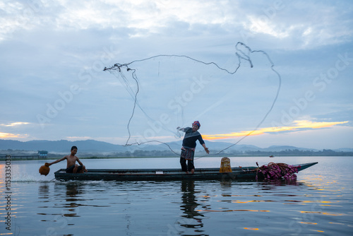 Fisherman casting his net at sunrise. Silhouette Asian fisherman on wooden boat casting a net in the Lake. Vietnamese Fisherman throwing net. photo