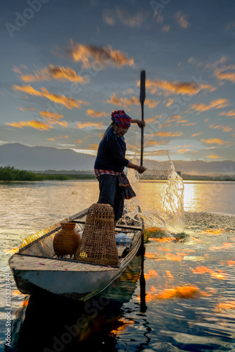 Fisherman casting his net at sunrise. Silhouette Asian fisherman on wooden boat casting a net in the Lake. Vietnamese Fisherman throwing net.