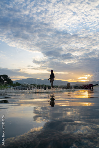 Fisherman casting his net at sunrise. Silhouette Asian fisherman on wooden boat casting a net in the Lake. Vietnamese Fisherman throwing net.