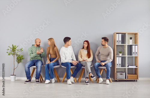 Group of five diverse young people sitting on chairs in row and talking to each other. Team of friends, students or colleagues discussing work or study matters, exchanging ideas and opinions together. photo