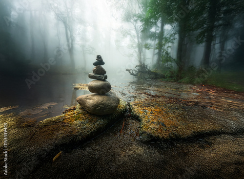 A serene stone stack meditatively placed by a misty forest stream.  The scene evokes peace and tranquility. photo