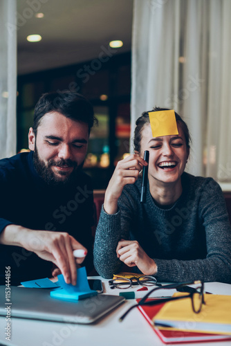 Joyful male and female sitting in campus and playing good positive game while waiting friends at cafeteria, successful caucasian studends having fun after doing homework indoors laughing at joke photo