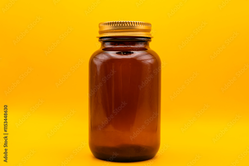 Amber glass jar with golden lid on yellow background Amber glass jar with golden lid on yellow background