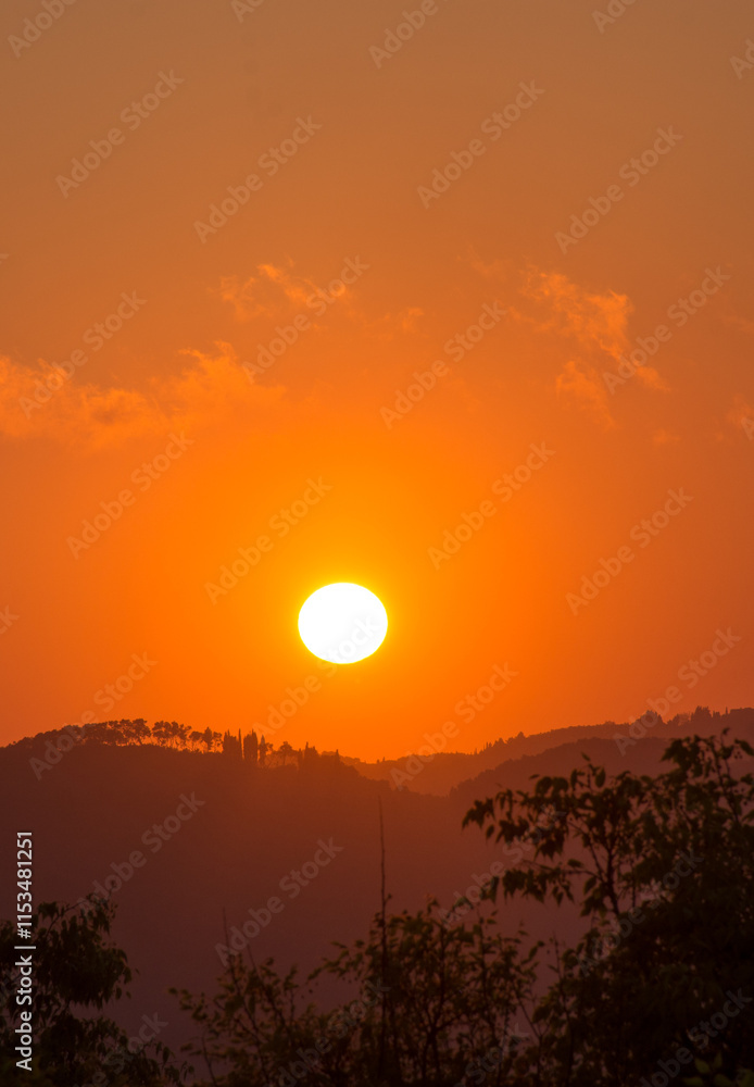 Sunset over rolling hills, vibrant orange sky, sun setting behind silhouettes of trees and mountains. Sunset over rolling hills, vibrant orange sky, sun setting behind silhouettes of trees and mountains.