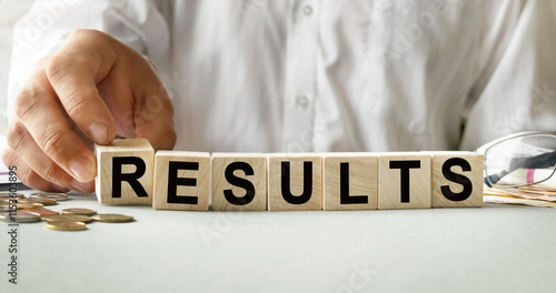 RESULTS inscription on the texture of wooden cubes. A business man holds a cube in his hand. An inscription on a financial, business or economic theme.