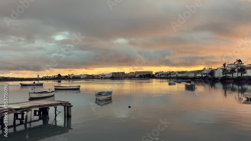 Tranquil sunrise illuminates barbate harbor in andalusia, spain, with fishing boats gently swaying on calm waters, reflecting the colorful sky and creating a serene coastal scene photo