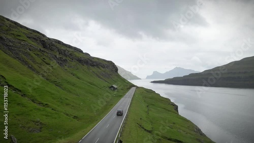 Breathtaking aerial shot of a car driving along a winding coastal road, surrounded by dramatic cliffs, lush green hills, and the vast expanse of the north atlantic ocean in Funnings, Faroe islands photo