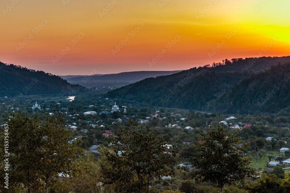 A beautiful sunset over a mountain range with a small town in the distance A beautiful sunset over a mountain range with a small town in the distance