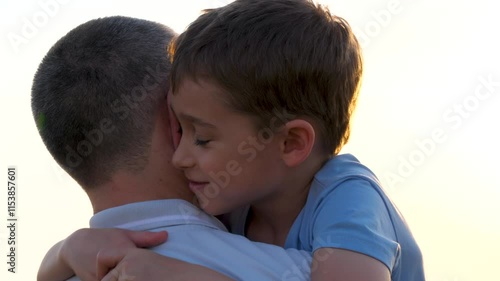 A happy boy lie on the shoulder, hugging his neck. Father and child spending time together at sunset. Father and son