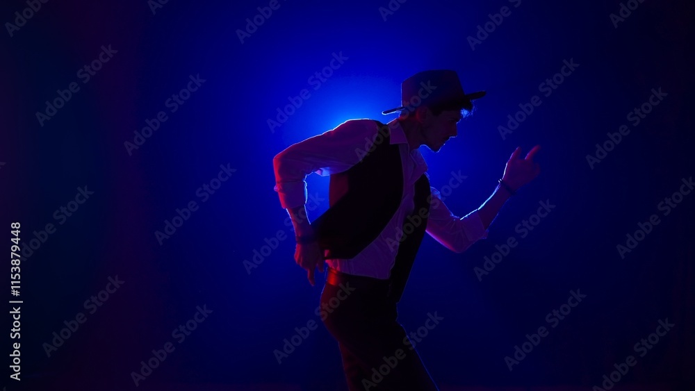 Man musician in stylish hat dancing on dark concert stage against blue spotlight and singing looking at camera, isolated on black studio background. Man musician in stylish hat dancing on dark concert stage against blue spotlight and singing looking at camera, isolated on black studio background.