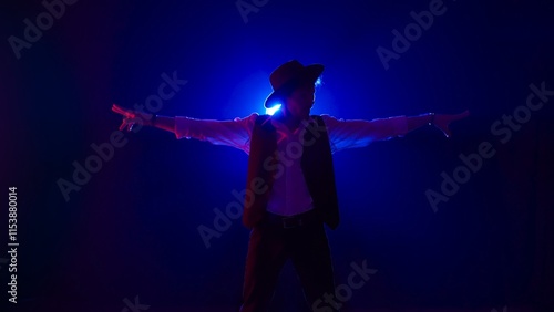 Sticker Man musician in stylish hat dancing on dark concert stage against blue spotlight and singing looking at camera, isolated on black studio background