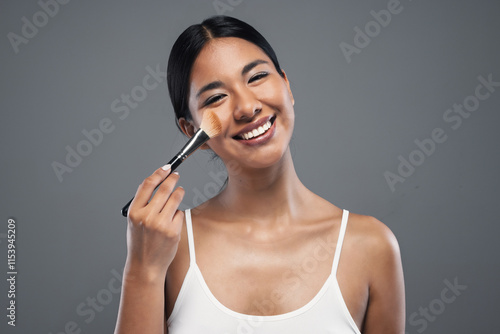 Beautiful young woman making make-up while looking at camera in isolated grey