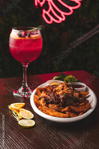 Foto Plato de chorrillana tradicional con papas fritas y carne junto a un cóctel de frutos rojos en copa de balón