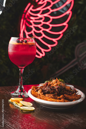 Bild auf Leinwand Plato de chorrillana tradicional con papas fritas y carne junto a un cóctel de frutos rojos en copa de balón