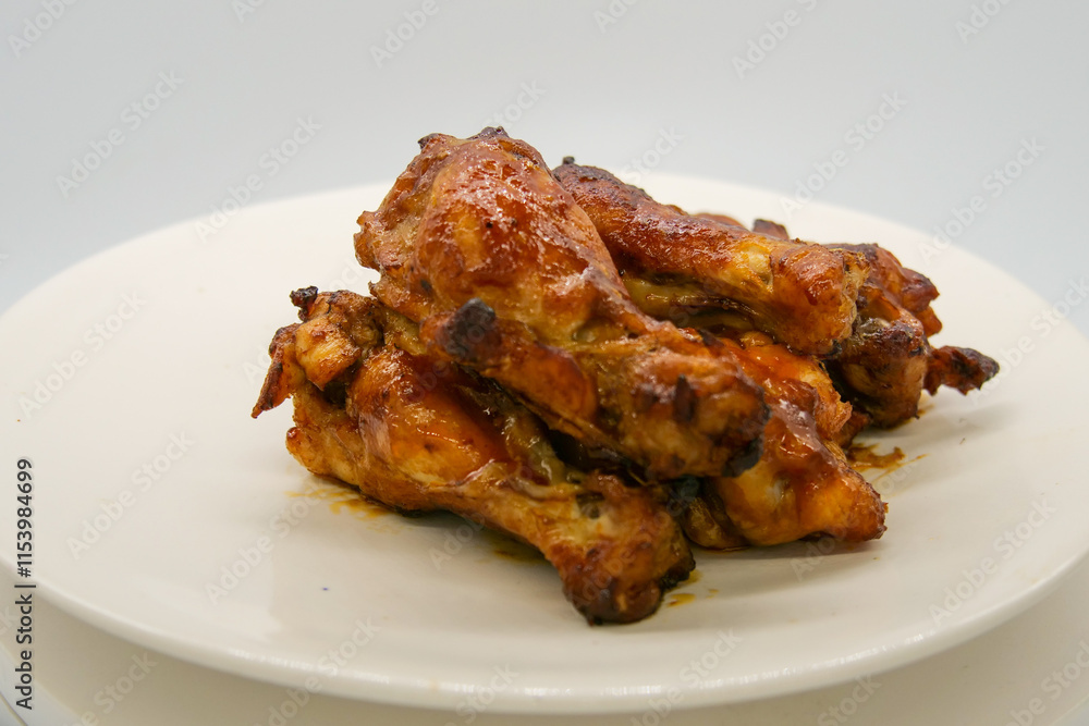 White plate with small brown basted and cooked chickenwings. White plate with small brown basted and cooked chickenwings.