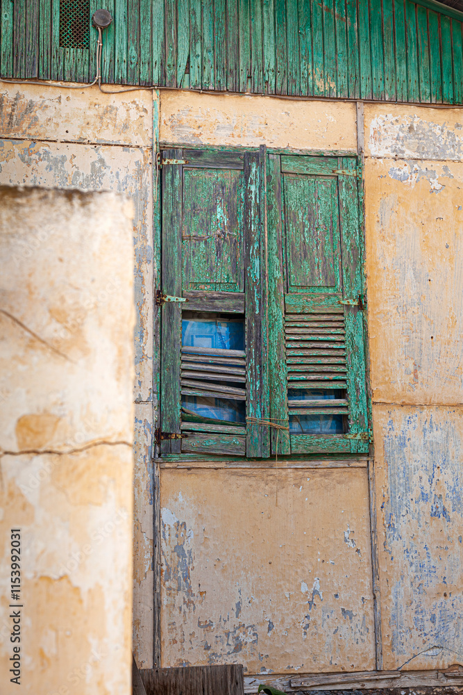 A rustic green wooden shutter on an old weathered wall in Lavrio, Greece, showcases the charm of decay with peeling paint and natural textures in the coastal town