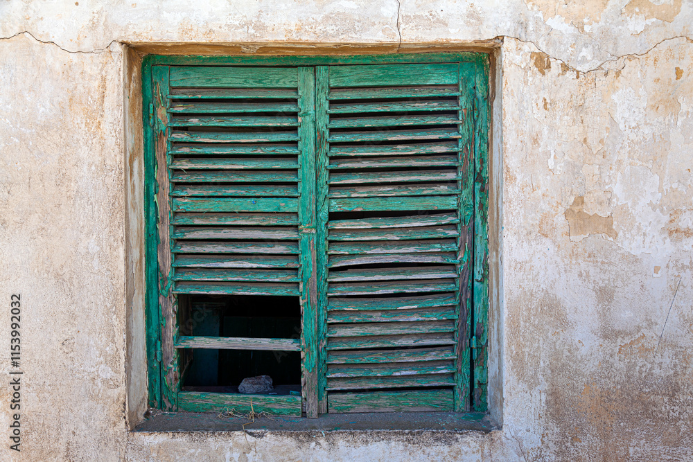 A rustic green wooden shutter on an old weathered wall in Lavrio, Greece, showcases the charm of decay with peeling paint and natural textures in the coastal town