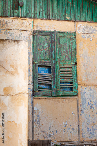 Obraz na płótnie A rustic green wooden shutter on an old weathered wall in Lavrio, Greece, showcases the charm of decay with peeling paint and natural textures in the coastal town w salonie