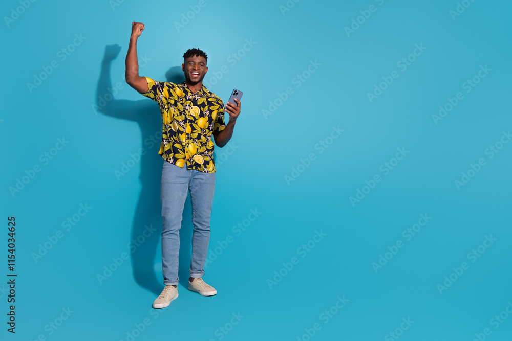 Joyful young man celebrating success on smartphone with a bright smile against blue background Joyful young man celebrating success on smartphone with a bright smile against blue background