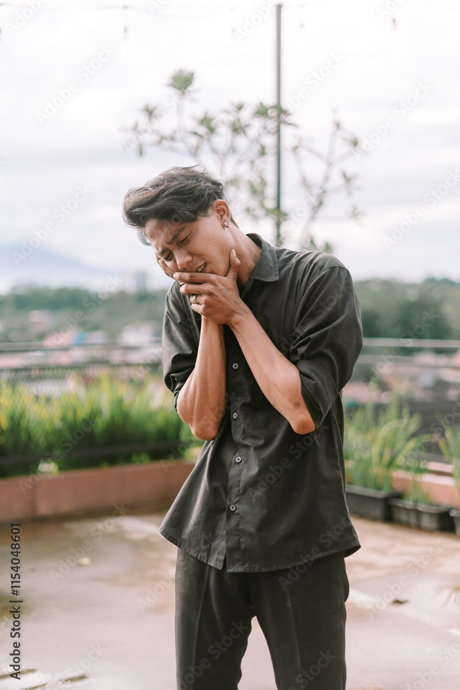 Southeast Asian man holding his cheek with a pained expression Southeast Asian man holding his cheek with a pained expression