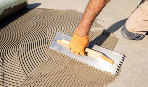 Foto Construction worker spreading tile adhesive on floor using notched trowel, prepa