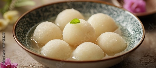 Delicious Rassgulla dessert served in a bowl featuring soft dumplings in light sugar syrup garnished with a mint leaf photo