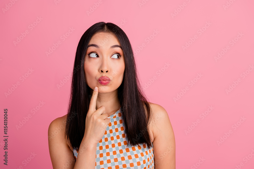 Young woman with contemplative expression against pink background, finger on chin, wearing trendy patterned top Young woman with contemplative expression against pink background, finger on chin, wearing trendy patterned top
