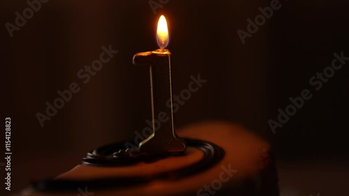 A cake with a minimum of details, decorated with one thin candle in the middle, the number 1. A hand brings a lighter to the candle and lights a fire. High quality 4k footage
