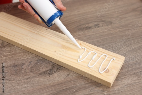Man with caulking gun glueing wooden plank at table, closeup