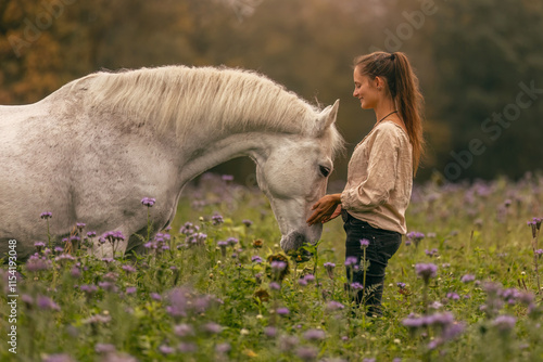 Bilde på lerret A young woman cuddle and interact with her white spanish horese on a wildflower