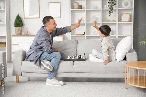 Cute little boy and his father with chessboard giving each other high-five on...