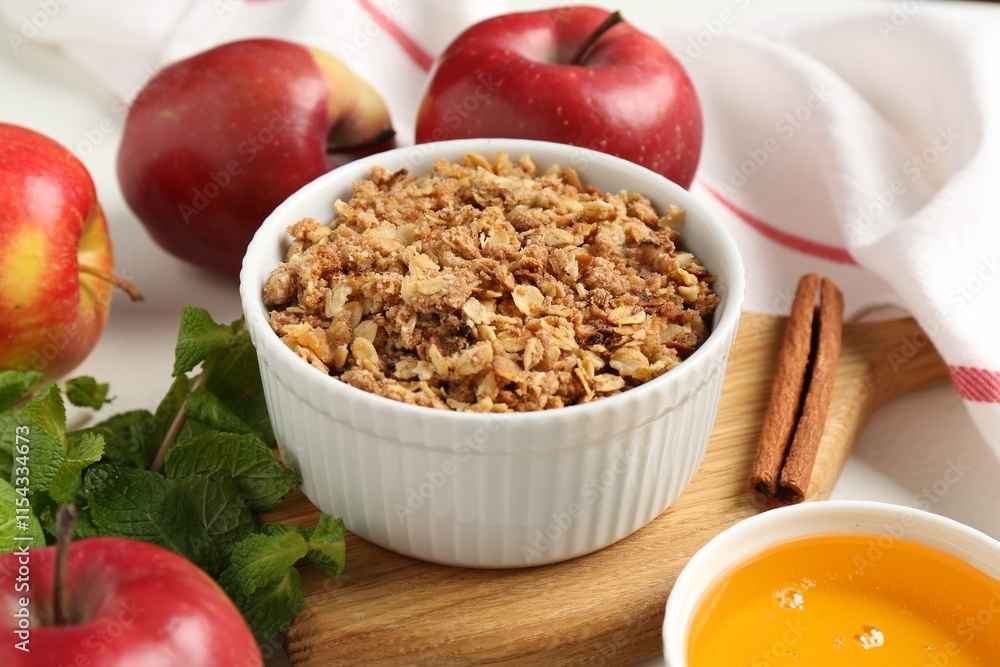 Delicious apple crisp in bowl, fresh fruits, mint, honey and cinnamon stick on table, closeup
