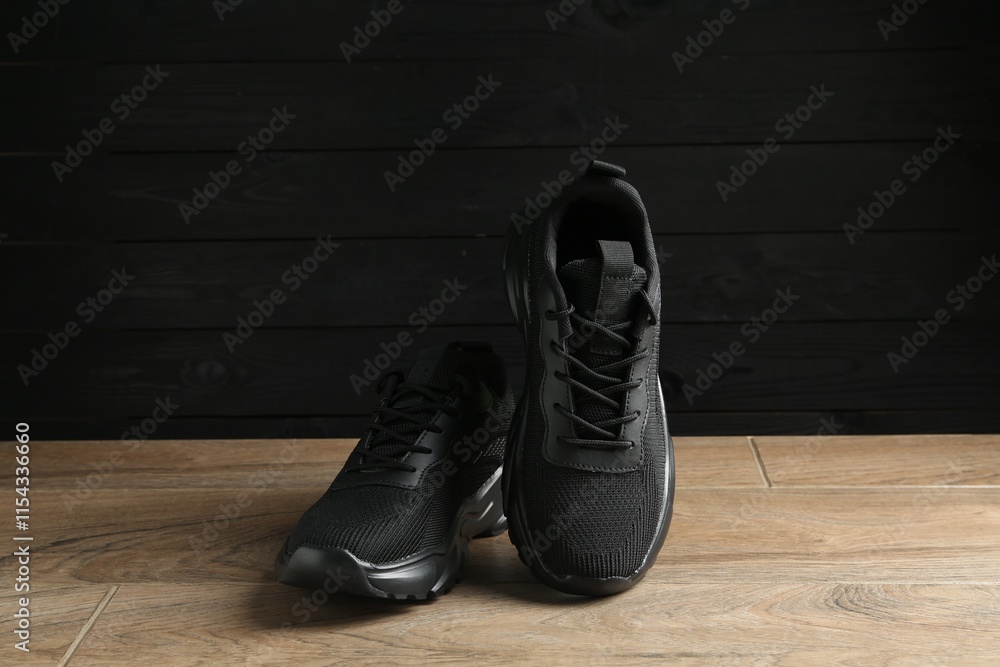 Pair of stylish black sneakers on floor against dark wooden background Pair of stylish black sneakers on floor against dark wooden background