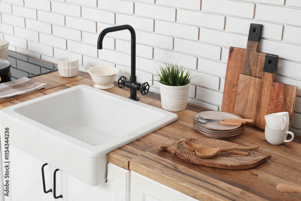Fototapeta premium White sink, chopping board and kitchen utensils on counter near white brick wall. Closeup