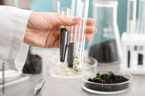 Female scientist holding test tubes with seedlings and soil in laboratory, cl...