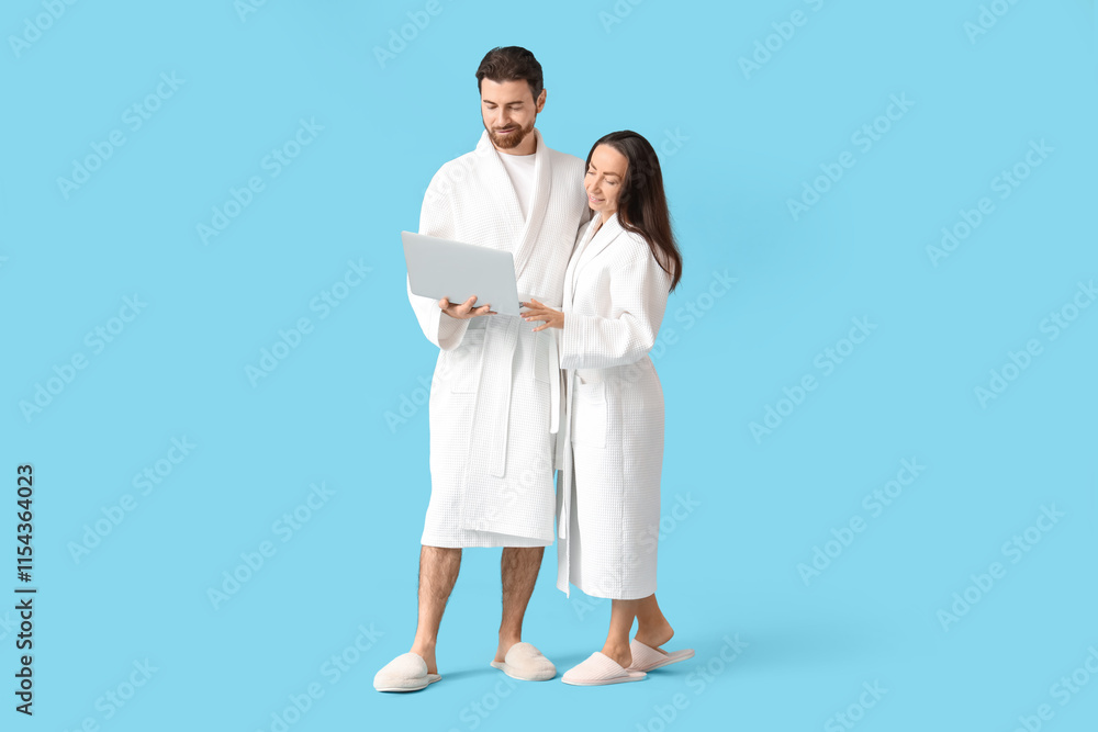 Loving couple in bathrobes using laptop on blue background Loving couple in bathrobes using laptop on blue background