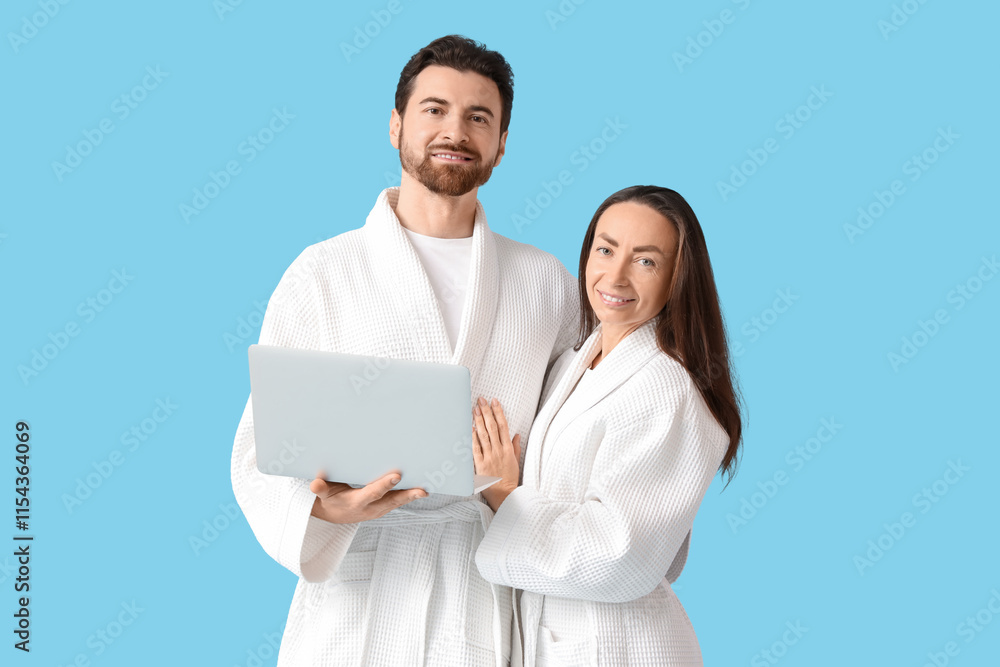 Loving couple in bathrobes using laptop on blue background Loving couple in bathrobes using laptop on blue background