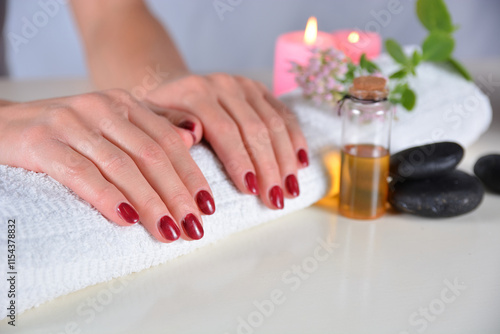 Female hands with red nail polish on a towel in a beauty studio, surrounded by decorations. Manicure and beauty concept