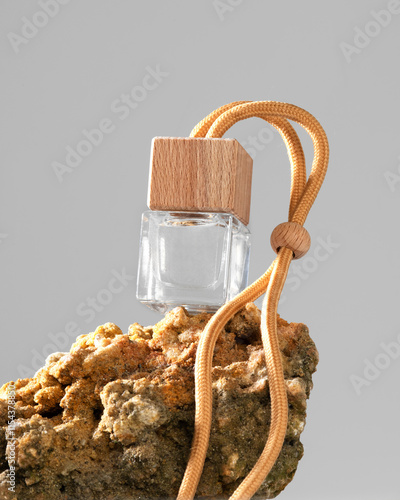 Car perfume in glass bottle with wooden cap on stone on light background
