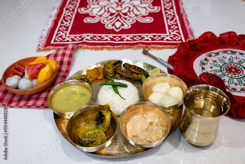 A festive or ceremonial Bengali meal served on a brass thali. Steamed white rice, dal, sorshe ilish or hilsa fish in mustard sauce, rosogolla, clay bowl containing fruit (watermelon, mango, lychee) photo