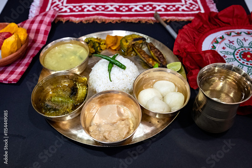 A festive or ceremonial Bengali meal served on a brass thali. Steamed white rice, dal, sorshe ilish or hilsa fish in mustard sauce, rosogolla, clay bowl containing fruit (watermelon, mango, lychee) photo