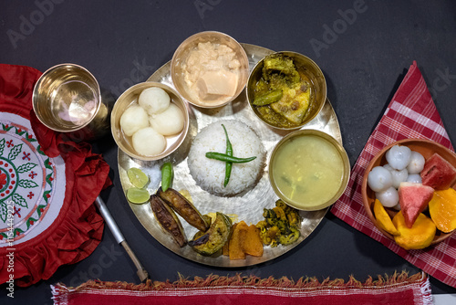 A festive or ceremonial Bengali meal served on a brass thali. Steamed white rice, dal, sorshe ilish or hilsa fish in mustard sauce, rosogolla, clay bowl containing fruit (watermelon, mango, lychee)
