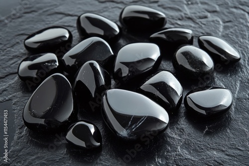 A collection of polished black obsidian tumbled stones on a dark surface.