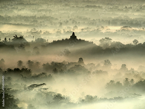 An aerial view of Borobudur Temple in a foggy and misty morning seen from Setumbu Hill using Tele Zoom lens to capture the beautiful nature and a sacred temple. photo