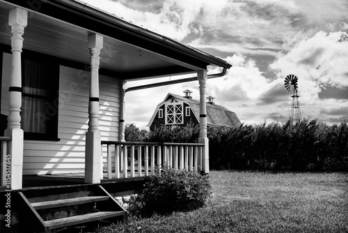 A black and white photo of a house with a porch and a windmill in the background