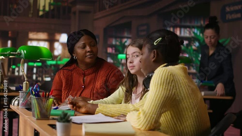 Black teacher mentoring her teen girls students with an assignment, teaching academic concepts and enhancing their knowledge through practical exercises. Private lessons at the library. Camera B.