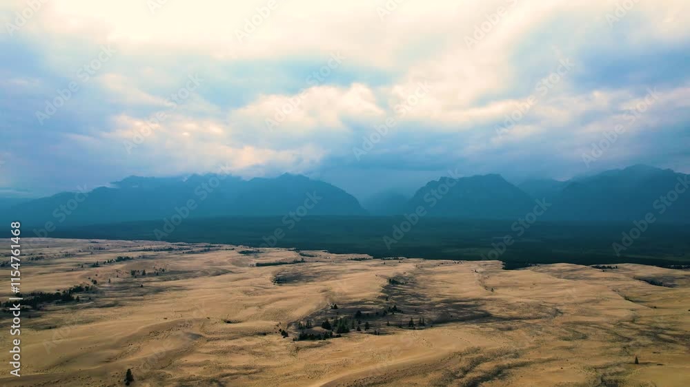 Aerial view of desert dunes leading to distant mountains under a cloudy sky Aerial view of desert dunes leading to distant mountains under a cloudy sky
