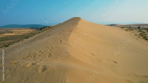 Drone flyover of a desert dune under a clear blue sky